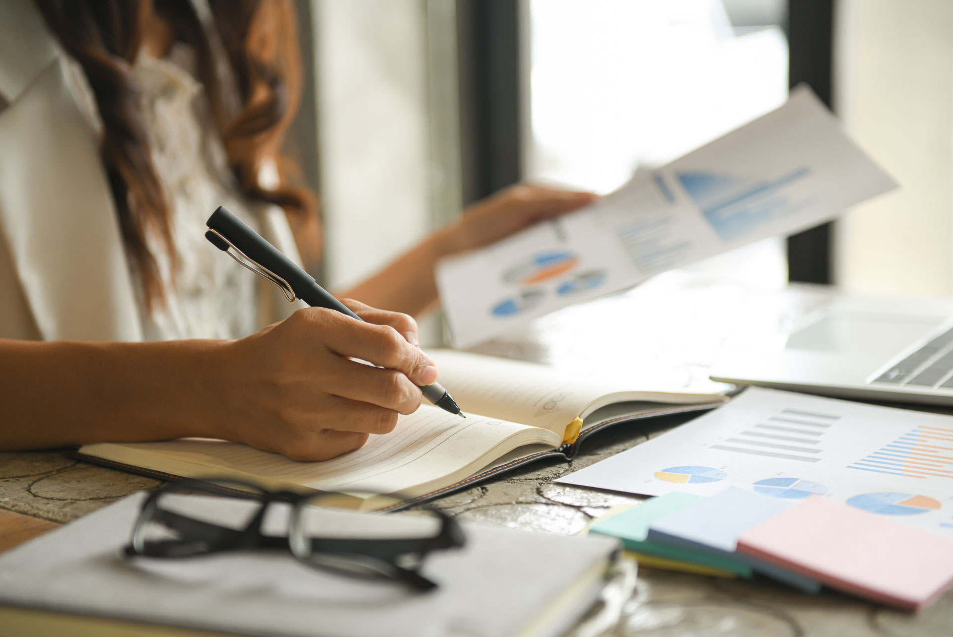 Manos de mujer escribiendo sobre un escritorio lleno de papeles